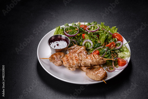 Pieces of chicken fillet baked on grilled wooden sticks with salad and red sauce