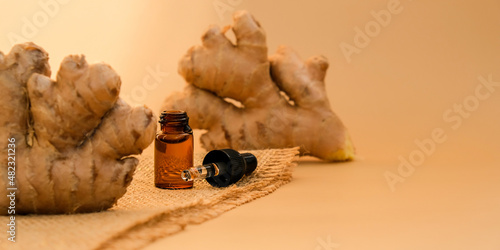Fototapeta Glass pipette of essential ginger oil, ginger root on beige background