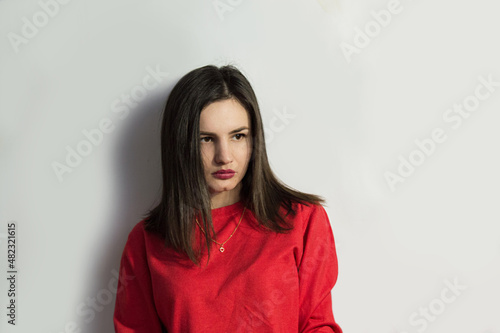 A beautiful beautiful young girl in a red sweatshirt looks mysteriously to the side, isolated on a white background. Emotion concept, with a cute smile. 