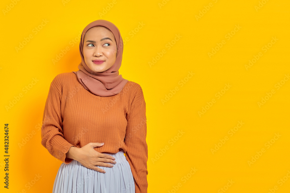 Portrait of happy young Asian woman keep hands on the stomach and feel satiety after eating tasty isolated on yellow background Portrait of happy young Asian woman keep hands on the stomach and feel satiety after eating tasty isolated on yellow background