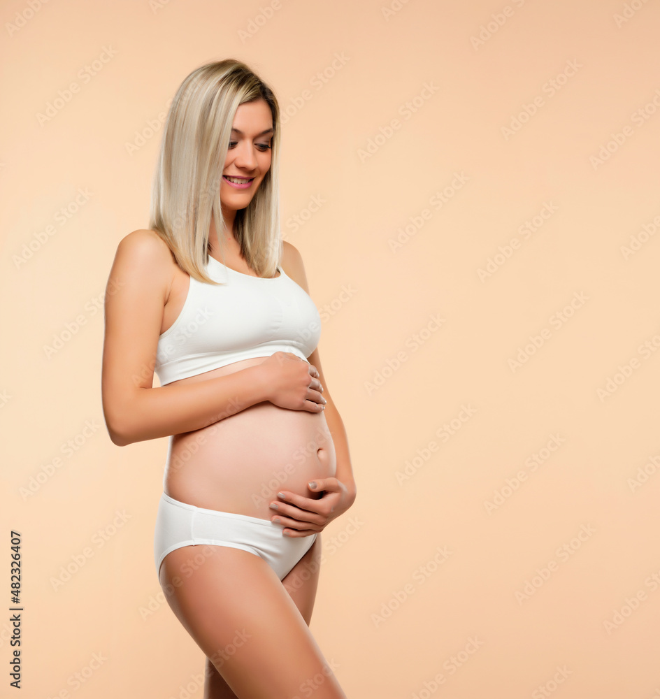 Young pregnent woman in lingerie posing on a beige