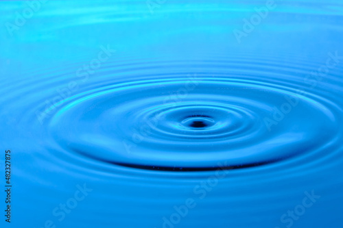 Bright blue background with diverging circles from dropped drop on surface water.