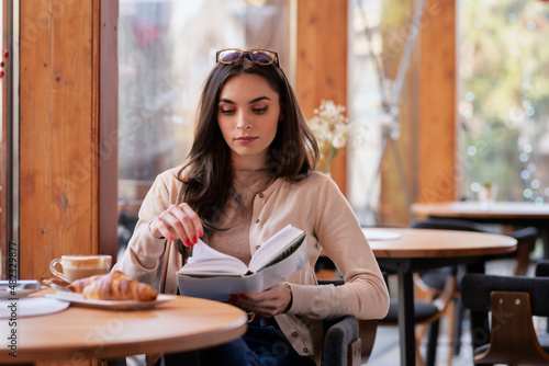 Beautiful young woman reading a book while sitting at the cafe