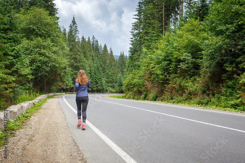 Young fitness woman running on the road through the forest. Slim girl jogging in the morning along the road.