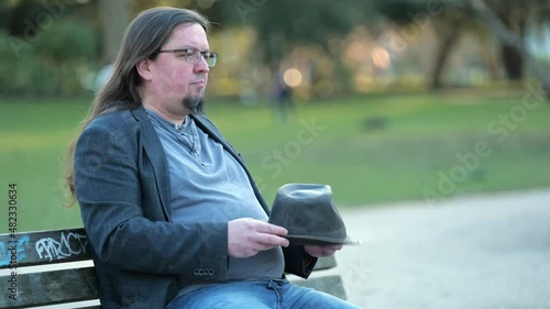 [4k] middle aged rocker sitting on park bench waiting playing with his hat