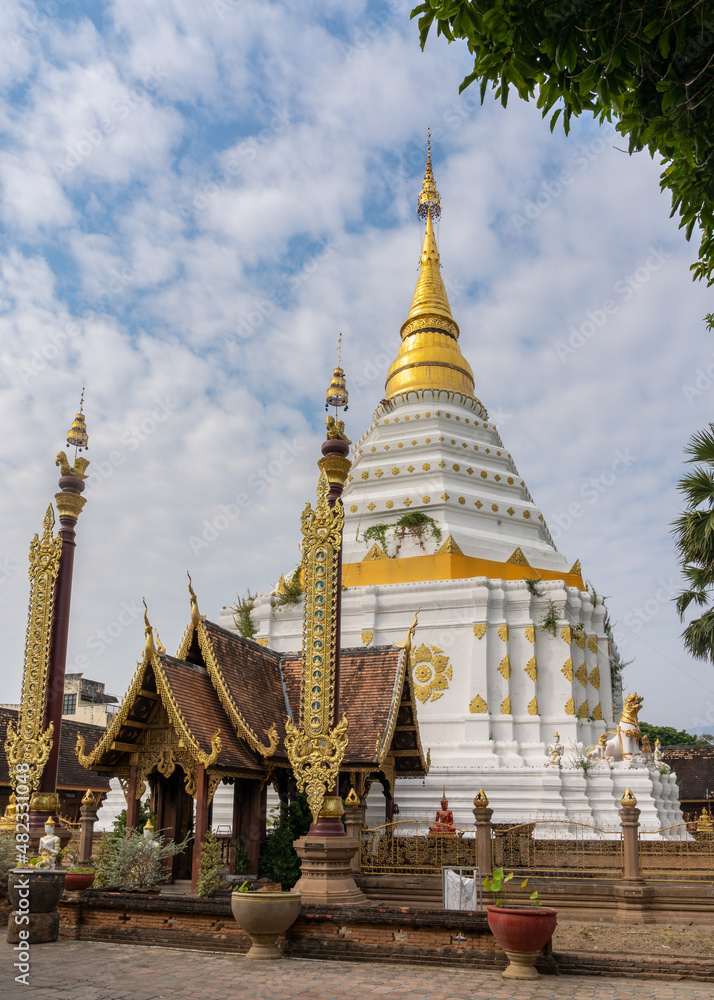 Landscape view of ancient octagonal stupa or chedi with wooden pavilion and traditional Lanna style banners in foreground at ancient Wat Chiang Yuen buddhist temple, Chiang Mai, Thailand