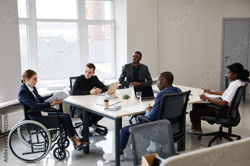 Portrait of successful businesswoman using wheelchair while leading business meeting in office with diverse group of people, copy space
