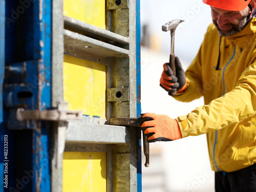 Worker hammering nail on formwork wall at construction site photo