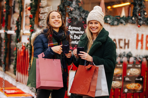 Cheerful friends with shopping bags enjoying mulled wine at Christmas market