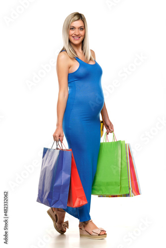 Young happy pregnant woman in long blue dress posing with a shopping bags