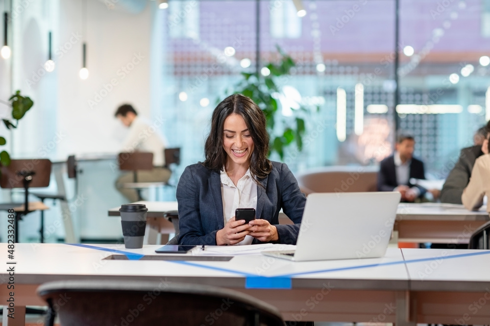 Smiling employee text messaging on mobile phone in office Smiling employee text messaging on mobile phone in office