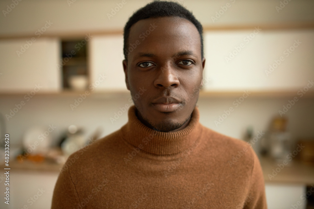 Fototapeta premium Head and shoulders close-up shot of attractive handsome brutal bearded dark-skinned male in brown wool turtleneck, looking at camera with confident positive face expression. Human appearance