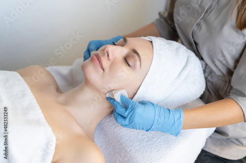 A young beautiful girl lies on the table at the beautician and receives facial cleansing procedures, makeup removal with white wipes