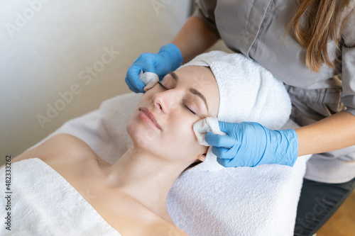 A young beautiful girl lies on the table at the beautician and receives facial cleansing procedures, makeup removal with white wipes