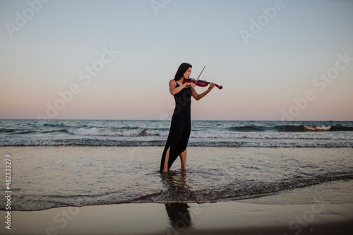 Woman playing violin in front of clear sky at sunset photo