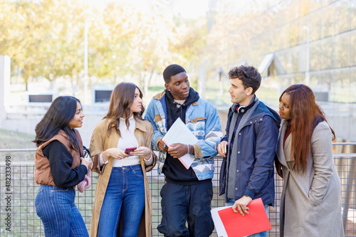 Multiracial students talking by railing at university campus photo