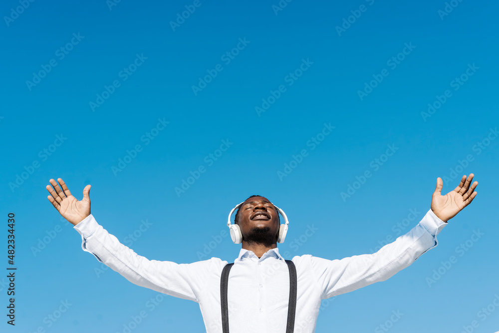 Man wearing headphones with hands outstretched on sunny day Man wearing headphones with hands outstretched on sunny day