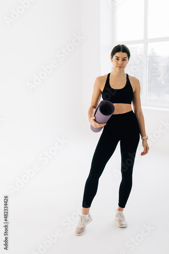 Beautiful smiling young girl in sportswear holding a yoga mat isolated on white background. Healthy lifestyle concept. Fitness and yoga concept.