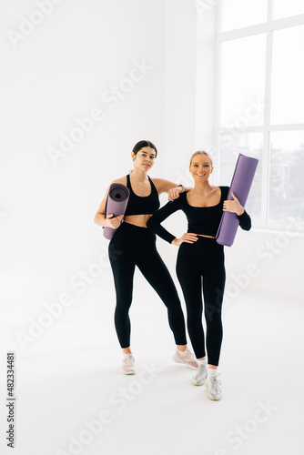 Two female friends in sportswear walk together with a yoga mats during yoga break at gym © F8  \ Suport Ukraine