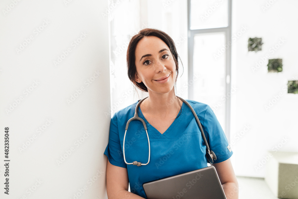 Smiling doctor with tablet PC leaning on wall in hospital Smiling doctor with tablet PC leaning on wall in hospital