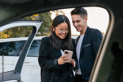 Smiling business colleagues sharing smart phone outside car photo