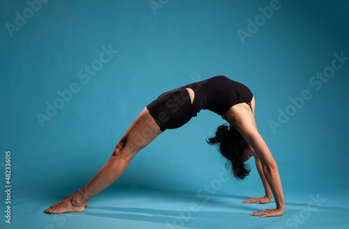 Athletic fitness woman standing in bridge position training body endurance working at healthy lifestyle in studio with blue background. Personal trainer exercising posture