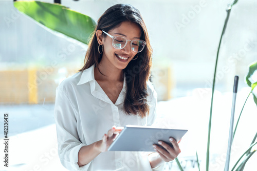 Smiling young businesswoman using tablet PC in front of window on sunny day photo