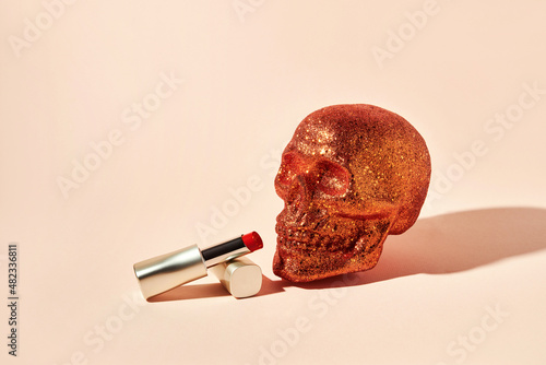 Orange skull covered with sequins and red lipstick on a beige background with copy space photo