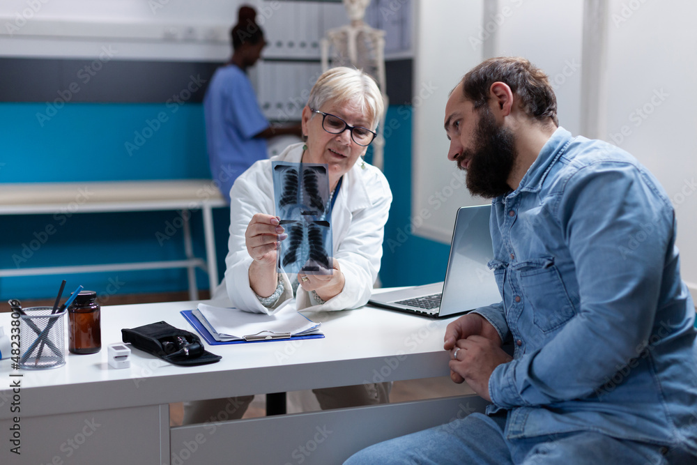 Medic holding x ray scan results for sick patient at checkup visit, explaining diagnosis and disease. Woman doctor analyzing radiography with man, giving medical addvice and support. Medic holding x ray scan results for sick patient at checkup visit, explaining diagnosis and disease. Woman doctor analyzing radiography with man, giving medical addvice and support.