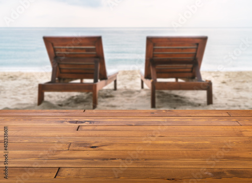 Beautiful brown plank wooden table or desk floor  little shiny surface  perspective view  the background of blurred sunbeds on the beach. Empty space for products to put on the table.