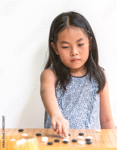 Portrait cute Asian child girl plays Go, the Japanese board game or Chinese board game, focus on the board game, white wall background, eyes on the game. photo