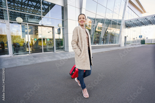 Cheerful lady walking away from airport with luggage