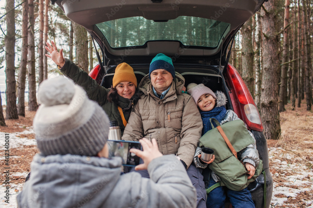 Winter family road trip. Happy parents with kids make photo in the trunk of car during walking in snowy pine forest, travel together in any season, active lifestyle, authentic people