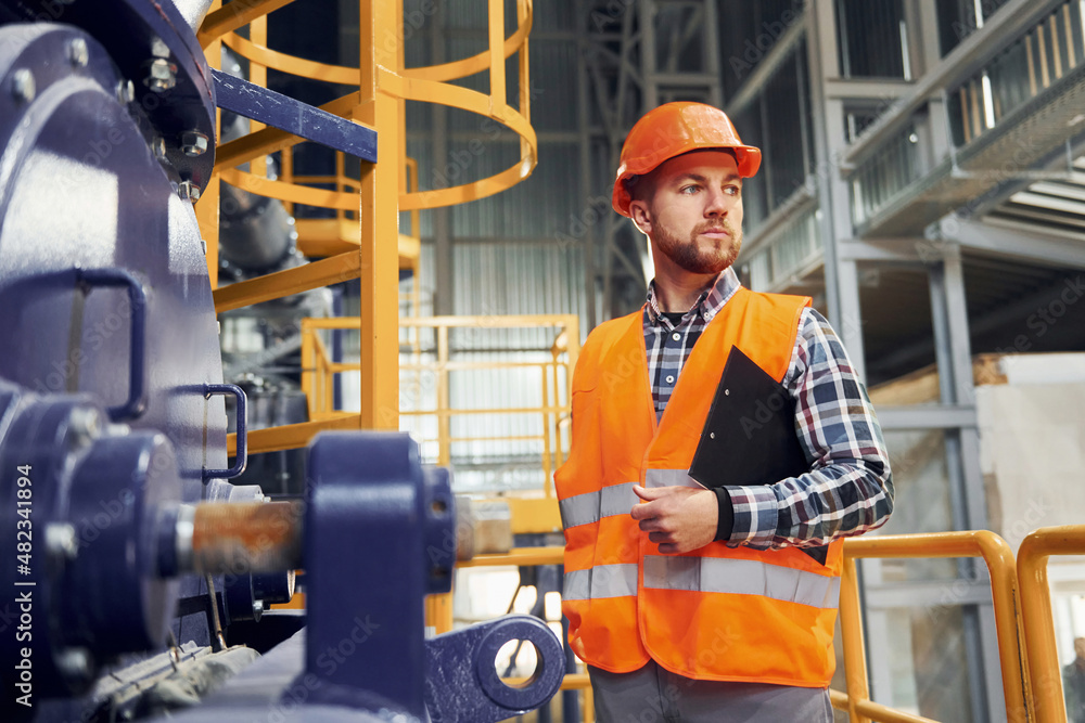 With notepad. Construction worker in uniform is in the factory With notepad. Construction worker in uniform is in the factory