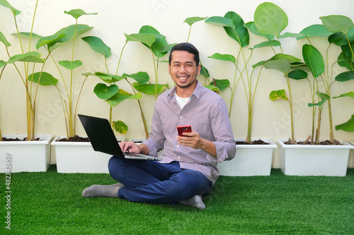Adult Asian man smiling happy when working using his laptop and mobile phone in the outdoor park photo