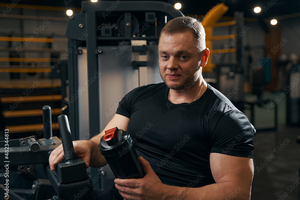 Athlete with healthy beverage seated on exercise machine Athlete with healthy beverage seated on exercise machine