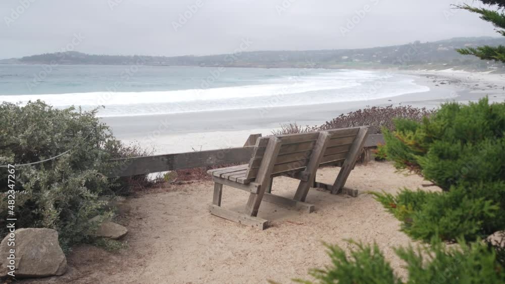 Empty wooden bench, rest on trail path, walkway or footpath. Carmel beach, Monterey ocean shore, California coast USA. Sea waves crashing. Waterfront beachfront pine cypress trees. Pathway or footway. Empty wooden bench, rest on trail path, walkway or footpath. Carmel beach, Monterey ocean shore, California coast USA. Sea waves crashing. Waterfront beachfront pine cypress trees. Pathway or footway.