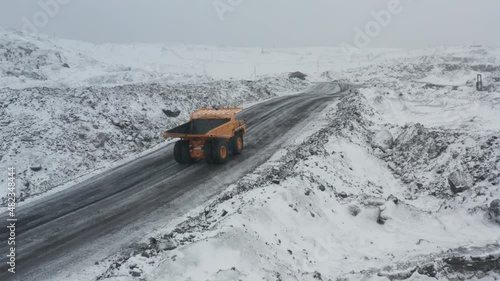 Large quarry dump trucks loaded with coal work at the coal mine in heavy snowfall.