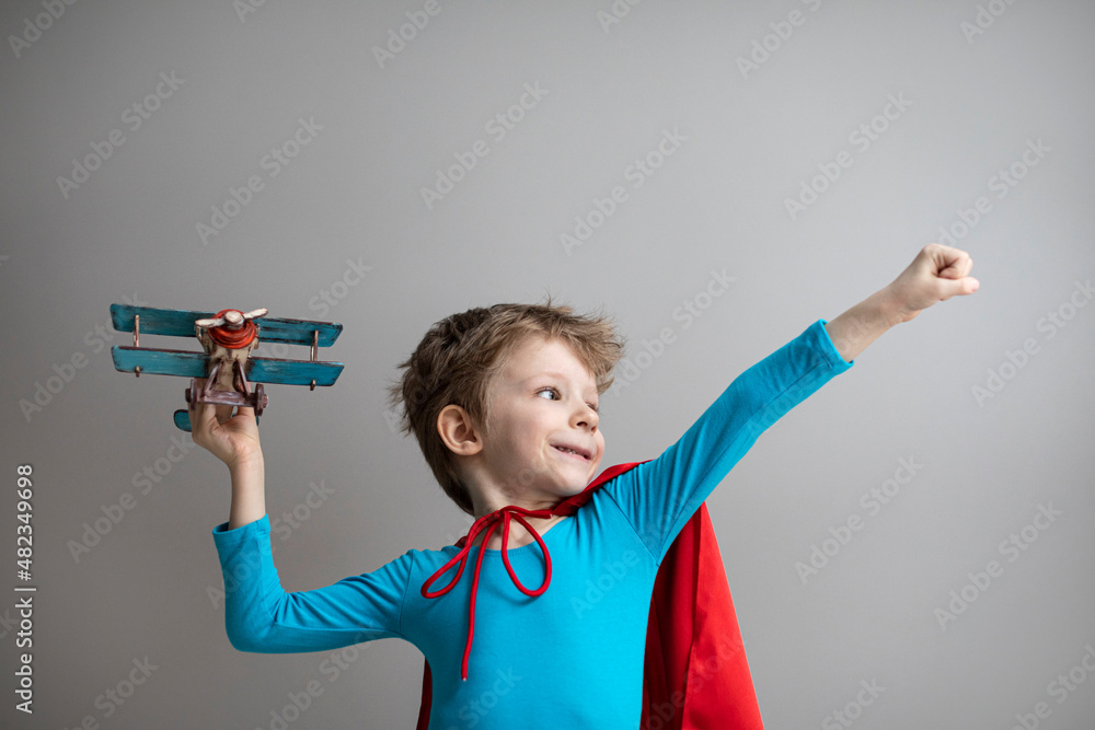 Little superhero boy in a red cape plays with an airplane. Happy smiling child. Success, motivation and travel. Little superhero boy in a red cape plays with an airplane. Happy smiling child. Success, motivation and travel.