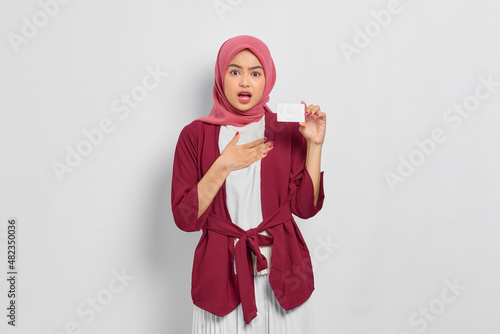 Shocked beautiful Asian woman in a casual shirt and hijab showing credit card isolated over white background. People religious lifestyle concept