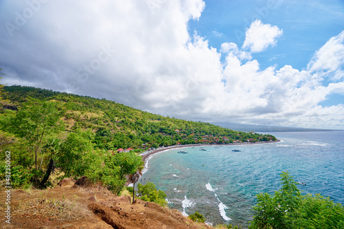 Beautiful landscape with ocean shore, green hill, cloudy sky. Amed Beach, Bali Island, Indonesia.