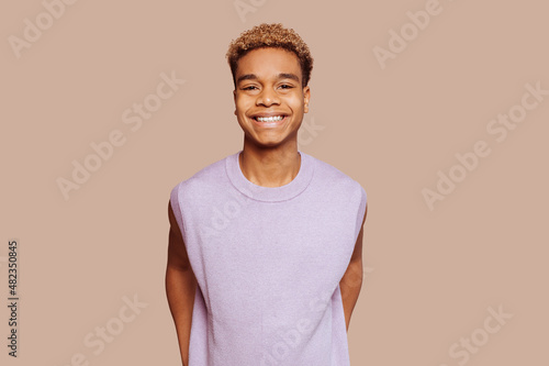 Cuadro en lienzo Glad young afro latin american black handsome man feels great, wears in purple top, broadly smiles and looks in camera stands over beige background