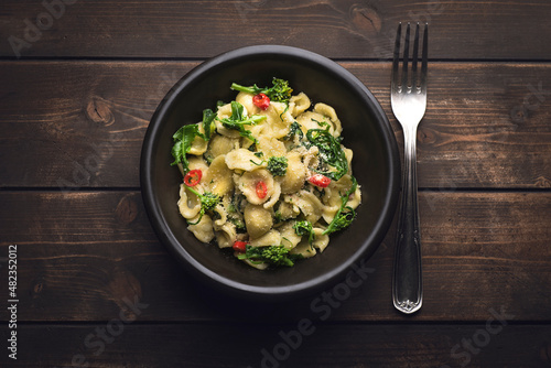 Italian pasta Orecchiette with turnip leaves (cima di rapa) and tops with garlic, hot pepper, grated bread on a dark wooden background. Recipes of southern Italy, Puglia. Poor cuisine, top view photo