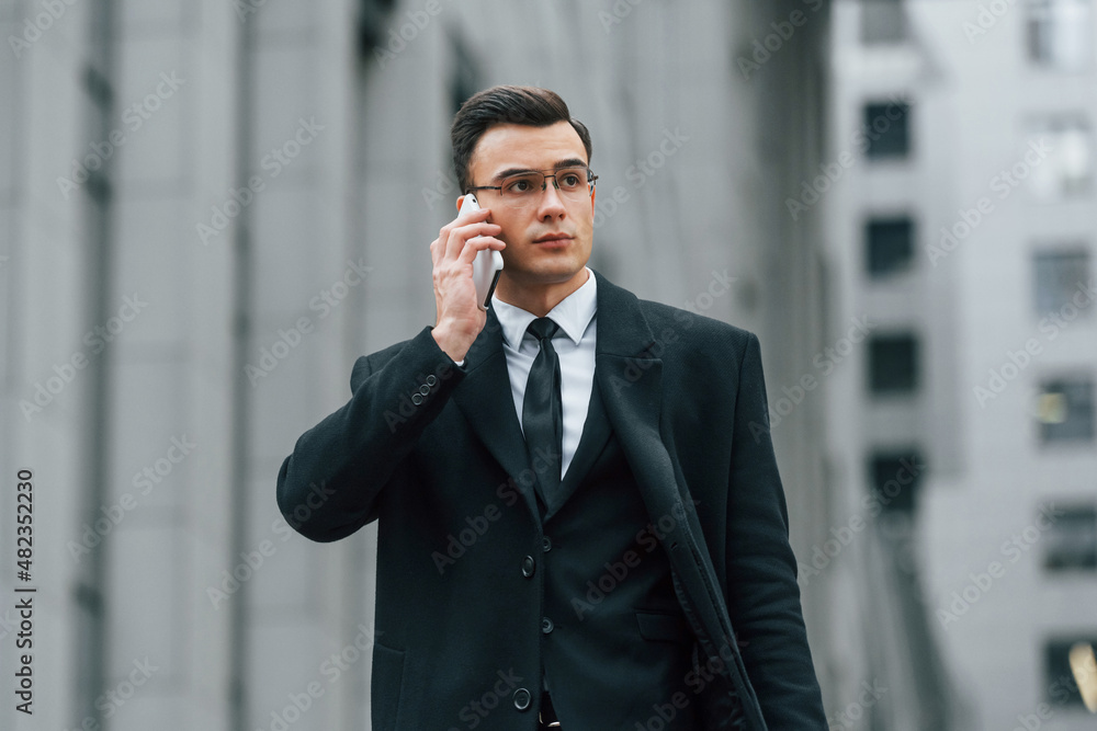 With smartphone. Businessman in black suit and tie is outdoors in the city With smartphone. Businessman in black suit and tie is outdoors in the city