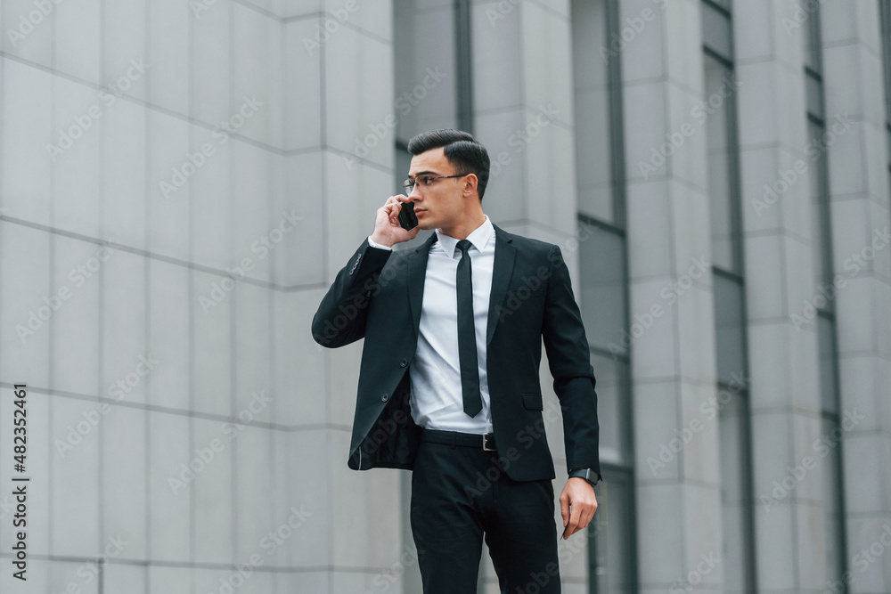 Using phone. Businessman in black suit and tie is outdoors in the city Using phone. Businessman in black suit and tie is outdoors in the city
