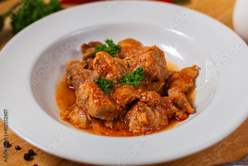 baked meat in slices in tomato red sauce in a white plate