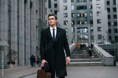 Front view. Businessman in black suit and tie is outdoors in the city