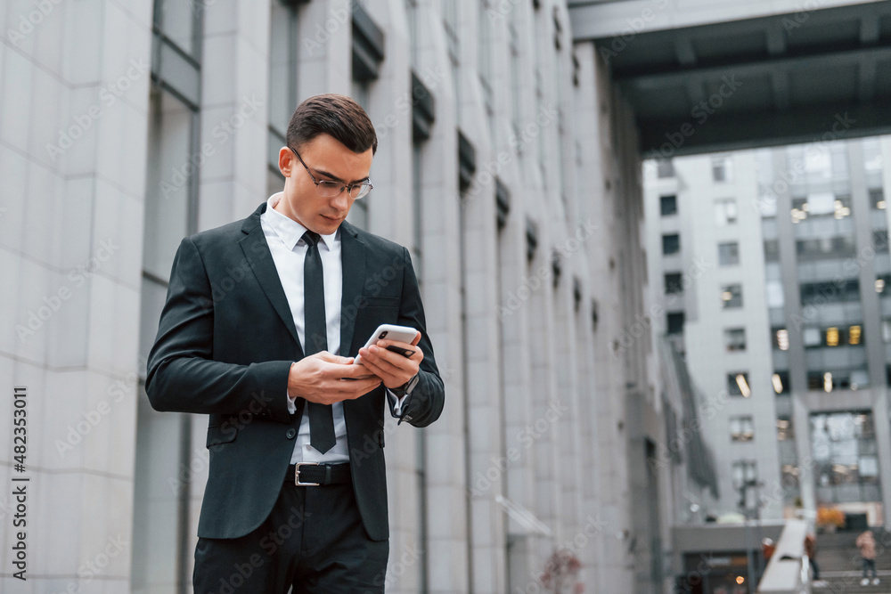 Busy man. Businessman in black suit and tie is outdoors in the city Busy man. Businessman in black suit and tie is outdoors in the city