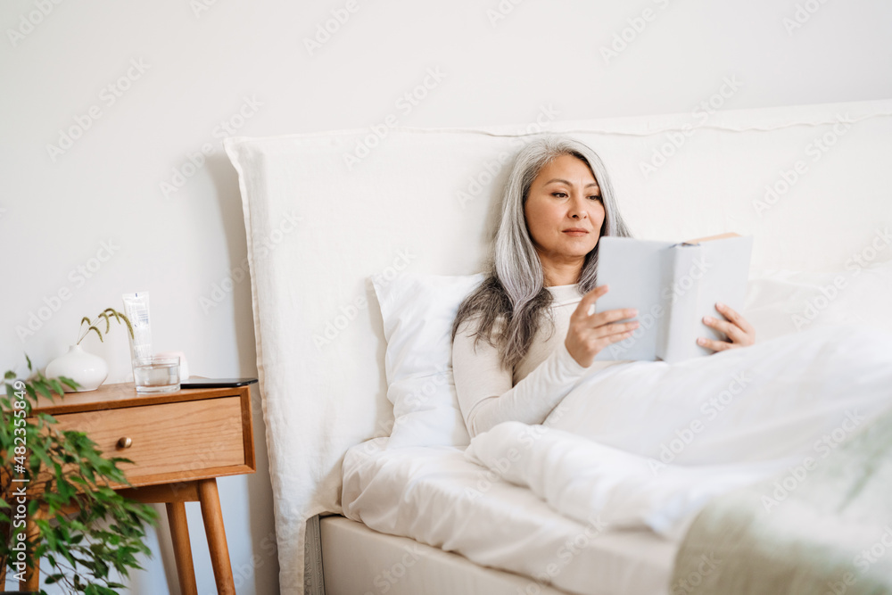 Grey asian woman reading book while lying in bed after sleep Grey asian woman reading book while lying in bed after sleep