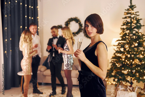 Standing near christmas tree. Group of people have a new year party indoors together